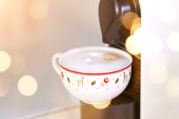 A cup of coffee in a coffee machine with Christmas lights