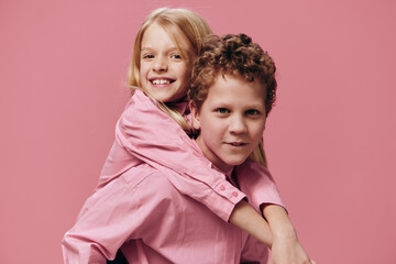 cute, joyful children play and the boy rolls his sister on his back in pink clothes on a pink background. Themes of relationships and friendship between children
