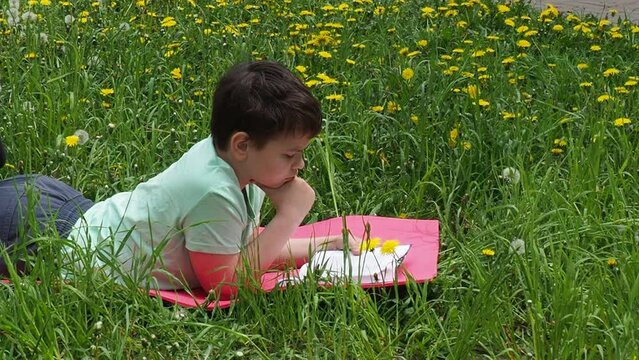 Young man in casual clothing lying on green grass and reading book in park on summer clear day. Inner freedom and happy lifestyle concept. boy summer vacation. hobby
