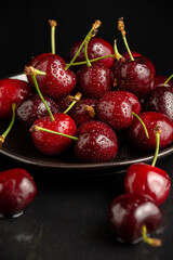 Top view of wet cherries on black plate, selective focus, black background, vertical