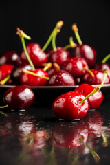 Focused closeup of wet cherries reflected on black background, selective focus, vertical