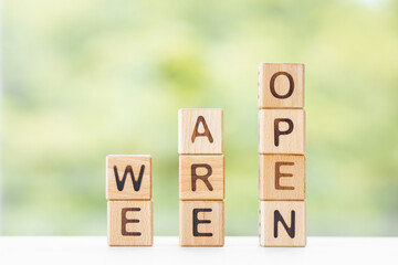 We are open word is written on wooden cubes on a green summer background Closeup of wooden elements