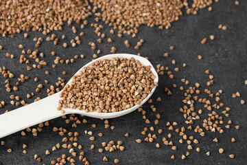 Uncooked buckwheat in a spoon on dark old boards. Buckwheat is used for cooking.