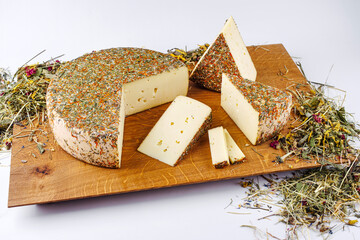 Traditional aged hay flower mountain cheese of the Alps offered as loaf and sliced on a wooden design board