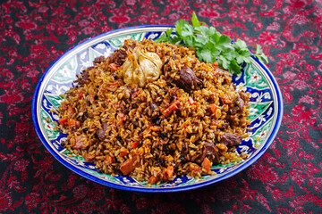 Traditional Uzbek fergana plov with devsira rice and lamb meat served as close-up on a handmade painted lagan platter