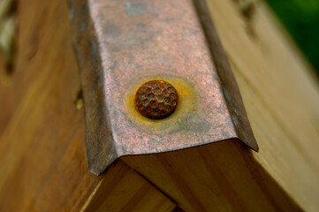 Close up photo of a rusty decorative nail on the top of the birdhouse. It's holding cooper part of the roof.