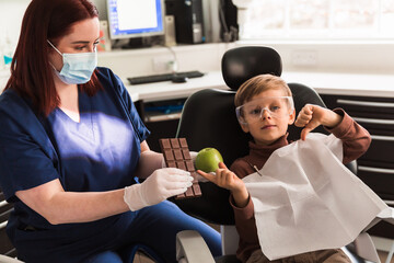 child boy  at pediatric dentist chair. little kids offers to choose a fresh apple, not sweet chocolate. concept is children's health.