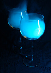 Two glasses with an alcohol vapors of vodka in a blue light on a dark background. 