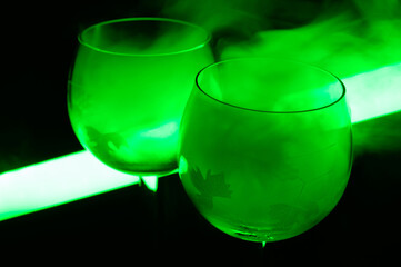 Martini cocktail covered with a smoke in a neon green light. Illuminating tube is glowing on a background.