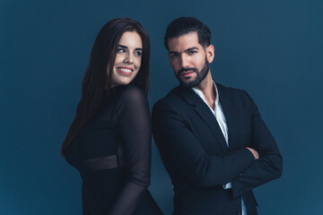 Two professional office people. Beautiful long-haired businesswoman and handsome businessman in a suit standing back to back in a studio over dark background. High quality photo