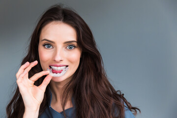 Close-up of orthodontic silicone transparent teeth aligner in female hands. A woman with a perfect charm smile holds a removable night retainer. Bracket for teeth whitening.
