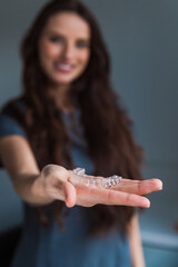 Close-up of orthodontic silicone transparent teeth aligner in female hands. A woman with a perfect charm smile holds a removable night retainer. Bracket for teeth whitening.