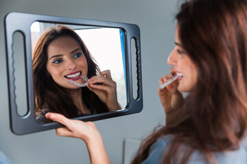 Young woman wearing plastic form for teeth alignment or whitening, looking to the mirror