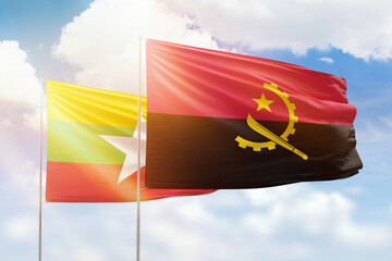 Sunny blue sky and flags of angola and myanmar