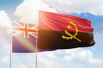 Sunny blue sky and flags of angola and new zealand