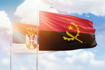 Sunny blue sky and flags of angola and serbia