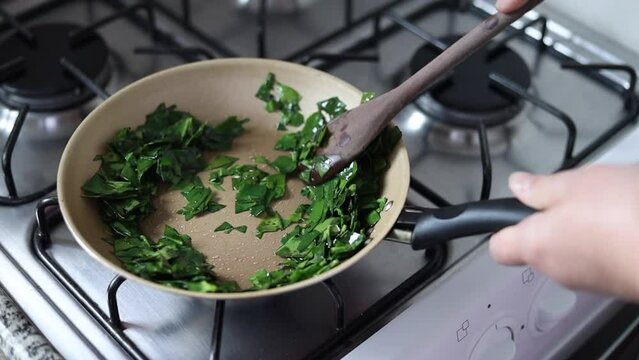 Hands cooking ora-pro-nobis (Pereskia aculeata) in a frying pan, a popular edible plant in Brazil