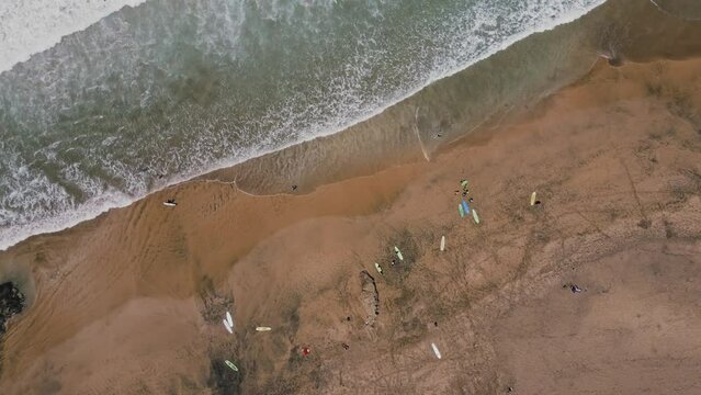 Bird's eye view on surfing beach with many surfboards in sand. Surfers enter the ocean walking through the waves. Sandy beach on a sunny summer day in Fuerteventura island. Canary Islands El Cotillo.