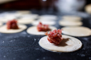 Preparation of a round shape from dough, a blank for dumplings. The minced meat is decomposed into blanks. Cooking on a black table. Flour. Close-up.