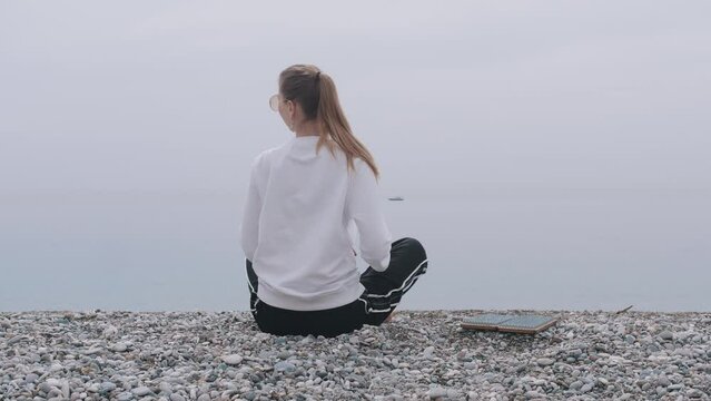 An inspired woman sits on the seashore in the lotus position and prepares to step on the sadhu board