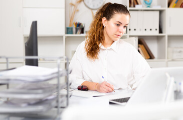 Focused young woman secretary working alone at her workplace on laptop