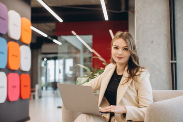 Young female entrepreneur using laptop in modern office corridor