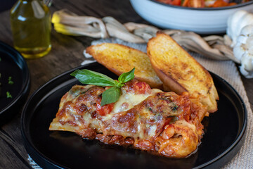 Meat lasagna with basil and bread in an elegant black plate