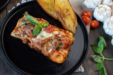 Meat lasagna with basil and bread in an elegant black plate top view