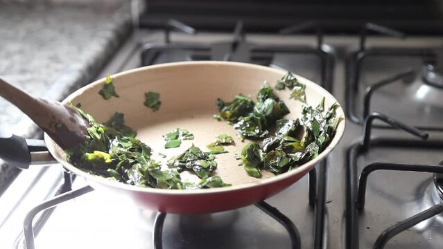 Hands cooking ora-pro-nobis (Pereskia aculeata) in a frying pan, a popular edible plant in Brazil