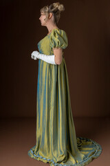 A blonde Regency woman wearing a green shot silk dress and standing against a plain backdrop