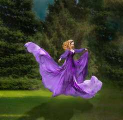 Woman with flowing purple dress floating in air with green trees in background. Magical...