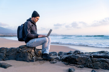 digital nomad working on his laptop outdoors from the beach at sunset