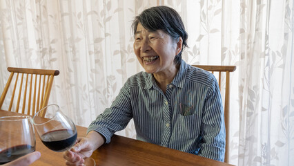 赤ワインの入ったグラスを持ち笑顔で乾杯する高齢者女性