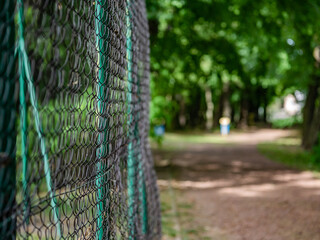 Fototapeta siatka w parku pośród drzew ogrodzenie boiska sportowego, zielone tło letni klimat zachodnia Polska obraz