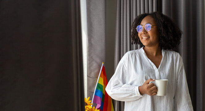 African American girl holding LGBTQ rainbow flag in her bed room for coming out of the closet and pride month celebration to promote sexual diversity and equality in homosexual orientation concept - Powered by Adobe