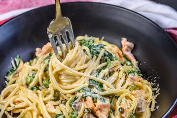 A close view of Salmon Spaghetti twirled around a fork in a dark round bowl