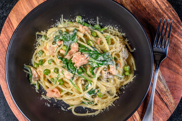 A serving of Salmon Spaghetti in a dark round bowl on a wooden background