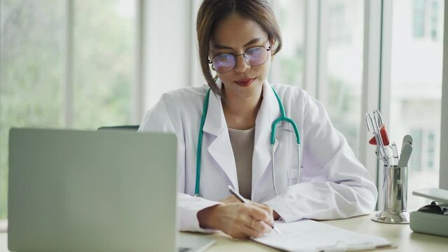 Attractive Female Doctor working with laptop computer and writing on paperwork,  female doctor make online video call consult patient on laptop, Medicine and health care concept