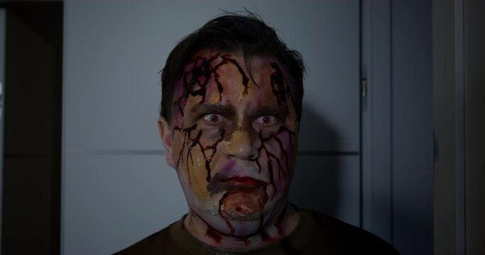Portrait of young man with braces who is turning into a zombie, so he is hungry. Newly converted walking dead man with bloody face and mouth screams and looks around wildly in search of food