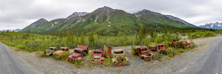 Rusty abandoned old trucks in vintage themed shot with boreal forest and mountains in background....