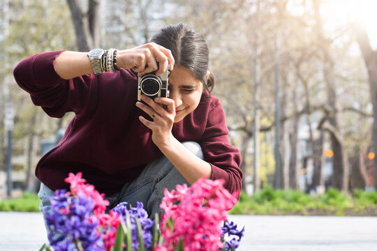 Young girl taking pictures of bright colorful spring flowers in park with film camera