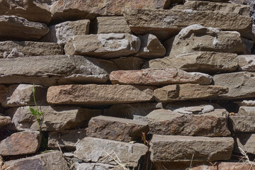The old wall is made of stone. Plastushki from natural natural material. Old cement lies on separate stones.