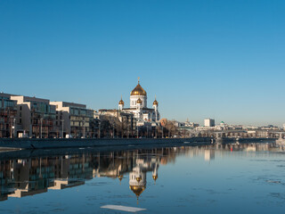 Fototapeta na wymiar Beautiful view of the embankment of the Muzeon Park and the Cathedral of Christ the Savior against the blue sky. Houses are reflected in the Moscow River. Copy space. Moscow, Russia