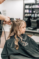 hands of a hairdresser with a curling iron make a hairstyle to a curly girl in a professional...
