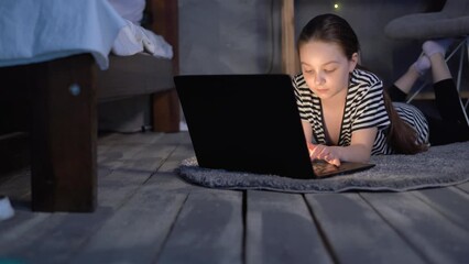 Little girl watching cartoons at night using a laptop, lying on the floor in the bedroom resting
