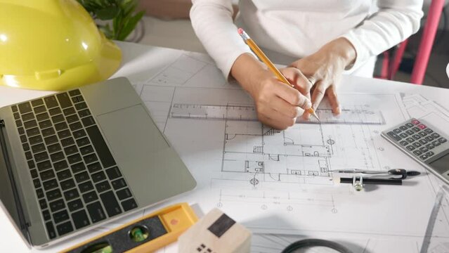 Architectural project workplace. Architect typing laptop keyboard to review design of house before editing drawing or sketching with ruler on plan blueprint paper on table desk at architecture office