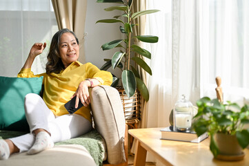 Happy asian aged woman resting in the living room, sitting on the comfortable sofa
