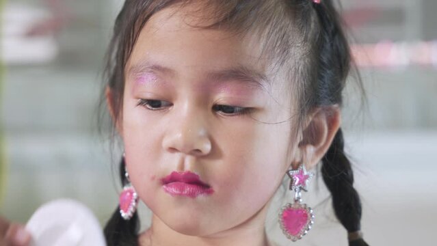 Asian adorable funny little girl making makeup her face she use blush puff pastry to cheeks, Learning activity to be woman, Close up face happy kid is beautiful make up with cosmetics toy