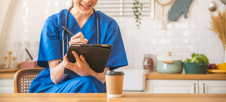 Young female doctor in work blue clothes dress with stethoscope sitting at the desk and use a pen to write on the iPad.
