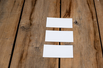 Three Blank business cards against a wooden background. White paper rectangles lie on top of old cracked boards. Selective focus.